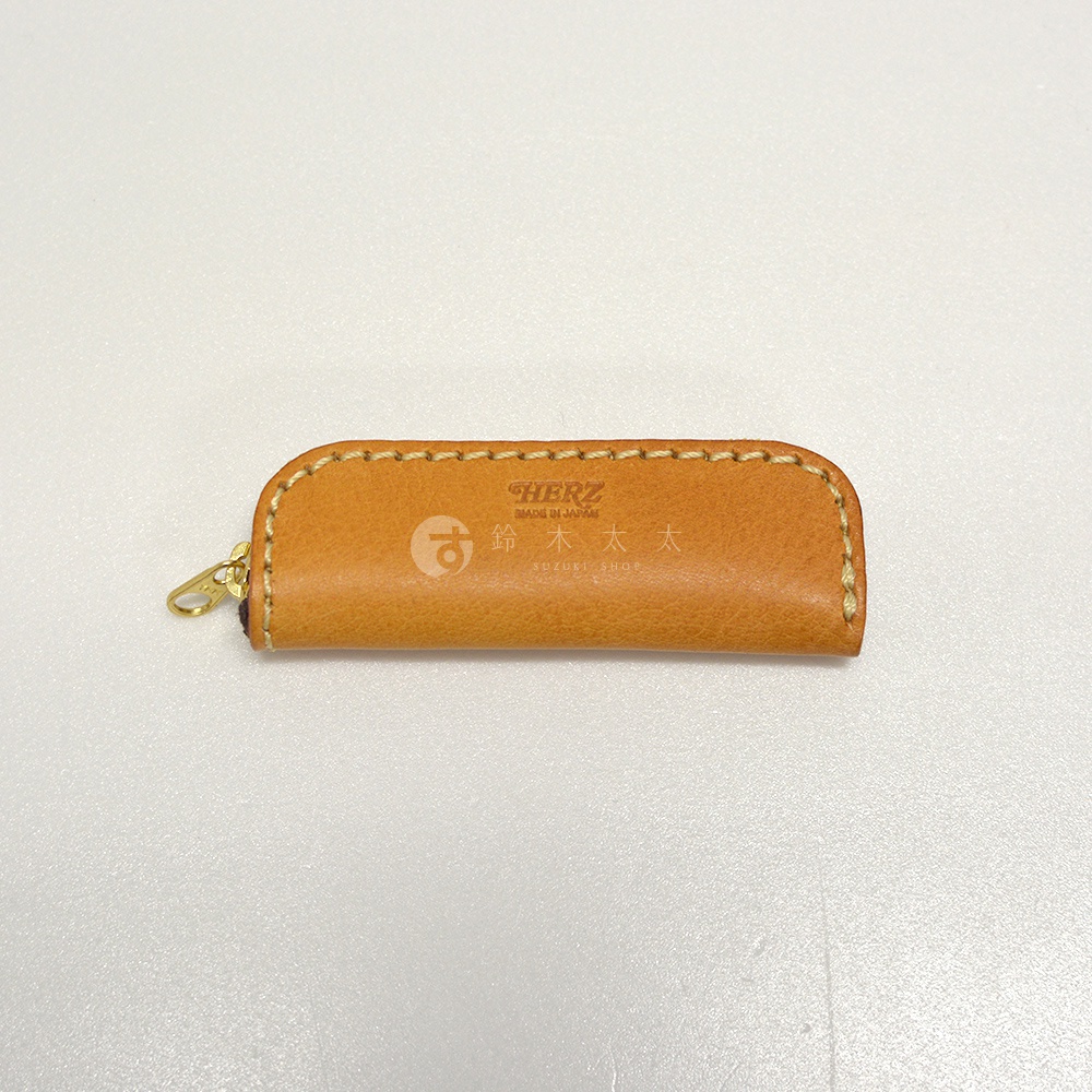 淺棕色皮革製成的職人手作印章收納袋，帶有縫線細節和金色拉鍊。袋面上印有「HERZ MADE IN JAPAN」及日文品牌名稱。