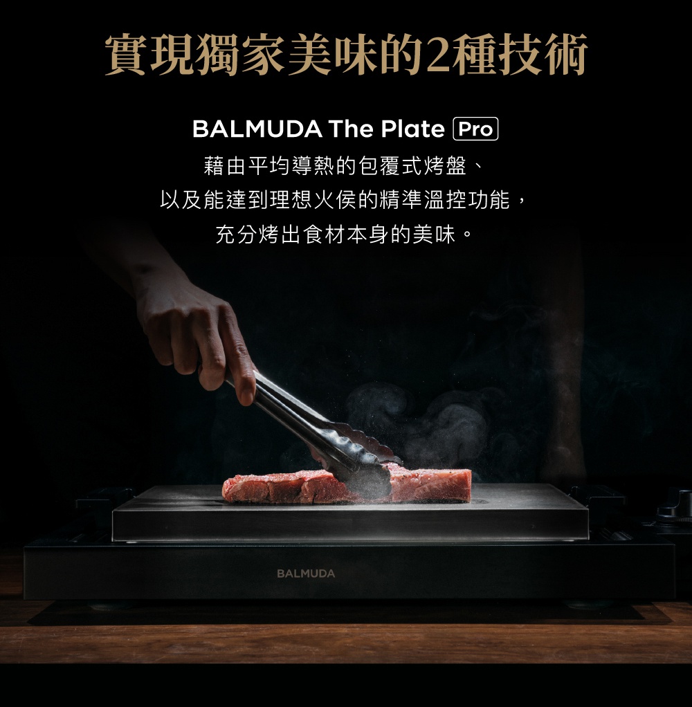 黑色 BALMUDA The Plate Pro 極致電烤盤，搭配夾子正在翻動兩塊牛排。烤盤表面呈現光滑的黑色材質，散發出烹調的熱氣。