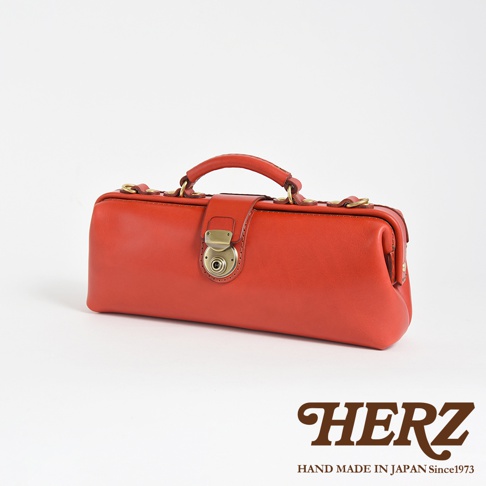 HERZ 職人手作紅色皮革橫長形杜勒斯單肩包，設有復古金色轉鎖和手提把，背景為白色。