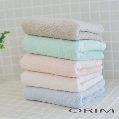 一疊 BISAI 今治浴巾，由上至下分別為淺灰色、薄荷綠、淡粉色、米白色與淺藍色，浴巾材質柔軟，堆疊擺放於白色磁磚背景上。