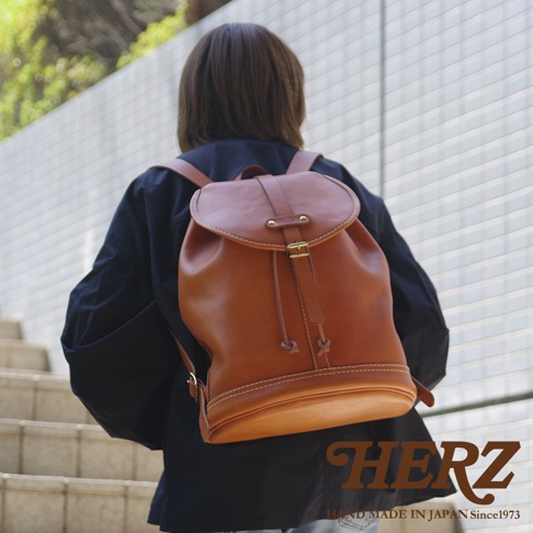 一名人士背著一個棕色皮革束口後背包，背包上有金屬扣環和抽繩，以及對比色的縫線。