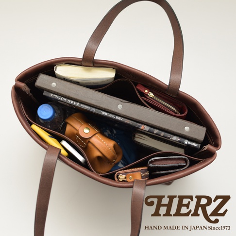 深棕色皮革極簡托特包，內部裝有書本、皮夾、水瓶、手機等物品，包包內有分隔層，展現其容量與收納功能。