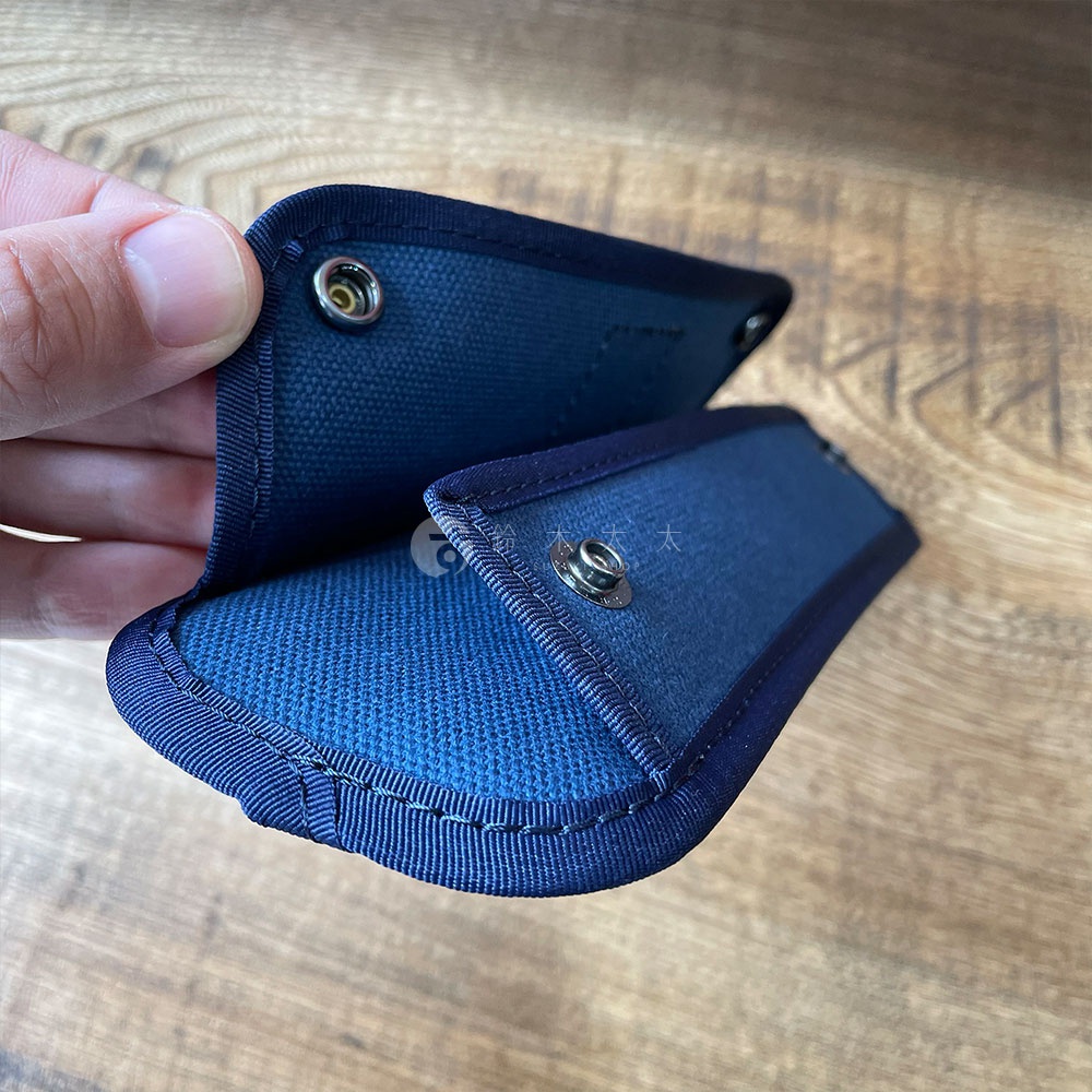 一對海軍藍純綿帆布肩墊，帶有金屬按扣，邊緣有縫線裝飾，由手指展示。