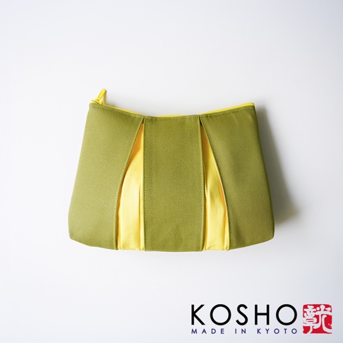 京都KOSHO品牌的一款ougi帆布化妝收納包，整體呈現橄欖綠與亮黃色的撞色拼接設計，外觀具有明顯的百褶紋理感，上方搭配亮黃色拉鍊，整體風格簡約優雅，右下角印有KOSHO MADE IN KYOTO及紅色印章標誌。