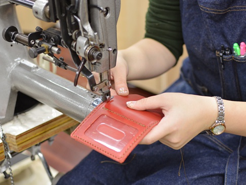 職人手作紅色皮革三面雙折票券收納夾，夾內有兩個透明夾層，正在工業縫紉機上進行縫製。