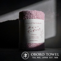捲起的一條淡紫色有機棉浴巾，標籤上印有日文和英文說明，包括「OBORO TOWEL」品牌字樣，尺寸約 60 x 120 公分，100% 純棉，日本製造。