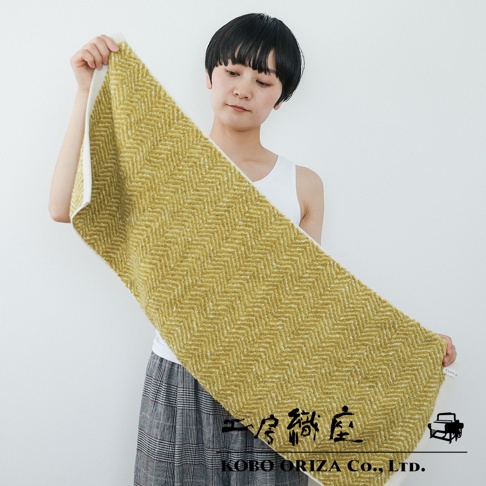 一款黃綠色棉麻混紡毛巾，以人字紋編織而成，質地柔軟，一側有白色滾邊。