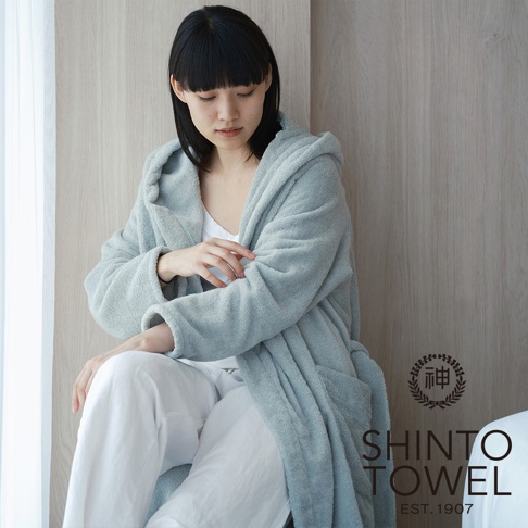 一位女性穿著一件淺藍色的連帽蓬鬆浴袍，搭配白色長褲。浴袍材質看起來柔軟，有著明顯的織紋。