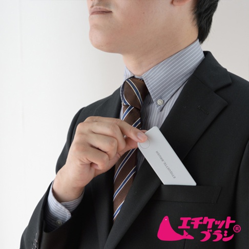 一位穿著西裝、襯衫和條紋領帶的男士，將一張白色長方形的免耗材隨身衣物除塵刷放入西裝外套的胸前口袋。