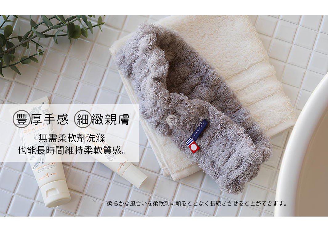 一件灰色毛絨絨的髮帶，上面有藍色和紅色的裝飾標籤，疊放在一條米白色毛巾上，背景是白色磁磚。