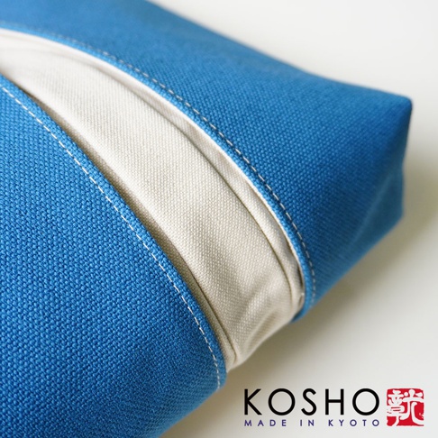 這是一個京都KOSHO品牌的ougi帆布化妝收納包特寫，採用厚實的藍色帆布材質，包身中央飾有米白色帆布拼接細節，邊緣配有精緻的白色車縫線，設計簡約優雅。