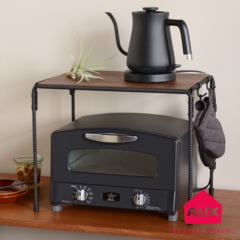 BOW 廚房工業風單層置物架，深棕色木紋檯面，黑色金屬鐵管支架，上面擺放一個黑色電熱水壺和一盆空氣鳳梨，下方放置一個黑色烤箱，右側掛有灰色隔熱手套。