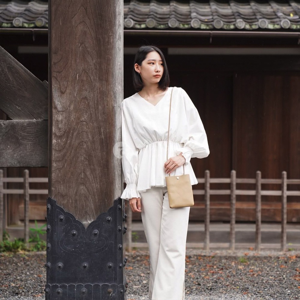 淺棕色皮革製的長方形手機包，附有細長肩帶，由身穿白色上衣及米白色長褲的模特兒斜肩配戴。