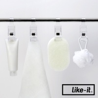 四個透明塑膠掛夾夾在金屬桿上，分別夾著一管白色乳液、一條白色毛巾、一個淺綠色浴球和一個白色網狀沐浴球。