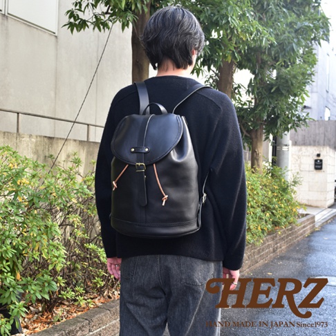 一位男性背著黑色皮革單扣束口後背包，背包有著束帶、金屬扣環和皮繩細節。