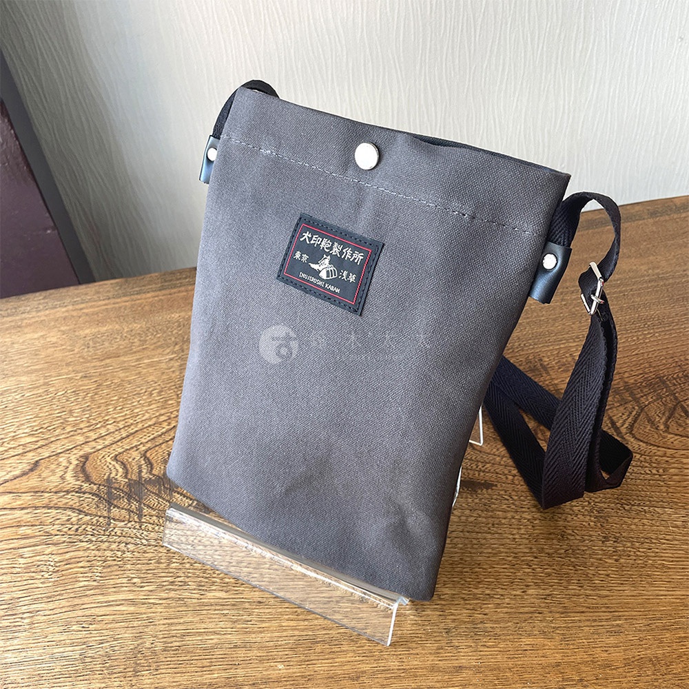 灰色帆布平板收納側背包，包身上有紅色標籤，標籤上有日文文字與圖案