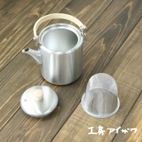 霧面不鏽鋼直筒茶壺，附有木質上弦把手，壺身為圓柱形，帶有細長壺嘴。另有同材質壺蓋及濾網。