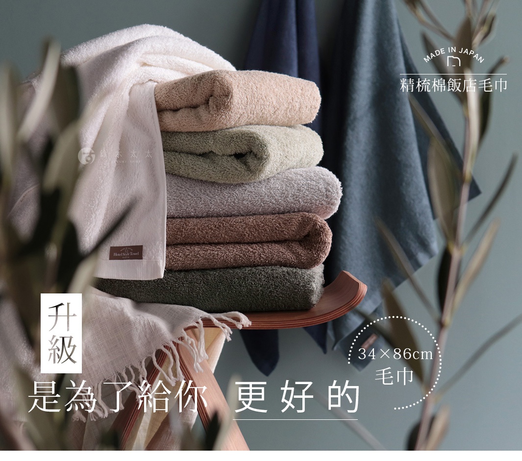 一疊由上至下分別為白色、淺褐、淺綠、灰色、棕色、深綠色的精梳棉毛巾，其中白色毛巾上有「Hotel Style Towel」標籤。背景為深藍色與灰綠色布料，右上方有「MADE IN JAPAN 精梳棉飯店毛巾」字樣，右下方標示「34×86cm 毛巾」。