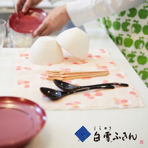 粉色友禪染布巾上擺放著兩個白色碗、兩支黑色湯匙及三支木製叉子，布巾印有粉紅色花朵圖案。