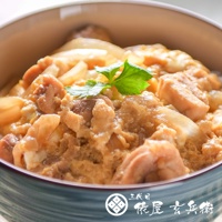 碗中盛有日式親子丼，碗內裝滿米飯、雞肉塊、炒蛋和洋蔥，淋上醬汁，表面裝飾著一片綠葉。