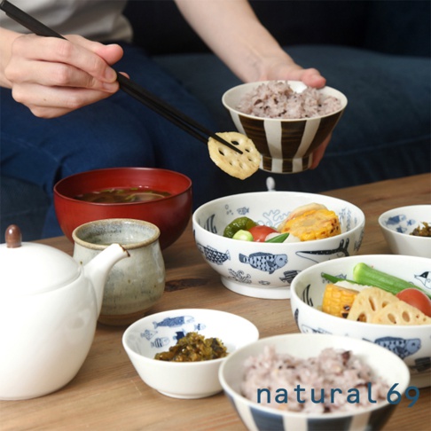 一套日本製陶瓷餐具，包含白瓷茶壺、紅色漆碗、淺灰色陶製茶杯，以及多個飾有藍色魚圖案的白色小碗，碗內盛有米飯、蓮藕、玉米、青椒等日式料理。