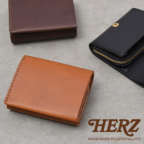 三款不同顏色的日本HERZ手工皮革雙折迷你短夾，分別以棕色、深褐色與黑色呈現，質感簡約洗練。圖片右下角標註HERZ品牌商標與日本手工製造字樣，展示出優質的皮革紋理與精緻的縫製工藝。