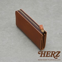 一個棕色皮革拉鍊長夾，上面印有HERZ品牌標誌和HAND MADE IN JAPAN Since1973的字樣