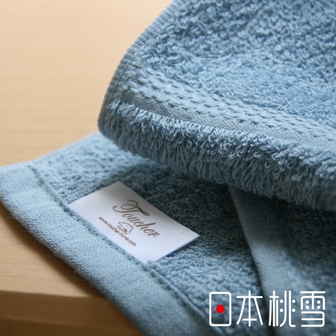 淺藍色純棉毛巾，觸感柔軟，帶有品牌標籤和精緻的織紋邊緣。