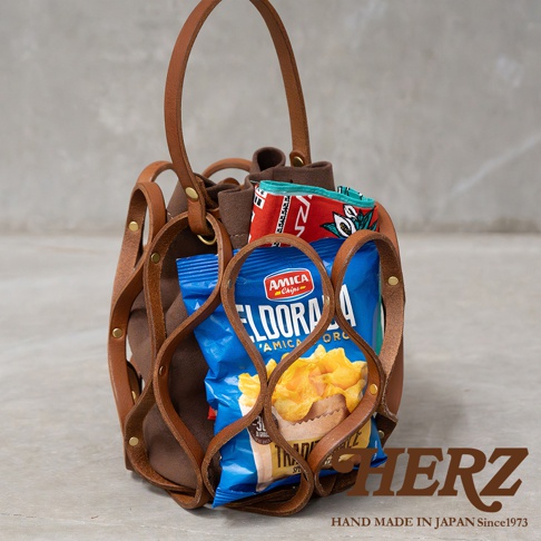 日本HERZ職人手作皮革Organ編織水桶包 G-98，包款細緻的皮革編織設計，內裝有Amica Chips的Eldorada洋芋片和印有圖案的布料，包包上的HERZ HAND MADE IN JAPAN Since 1973標誌。