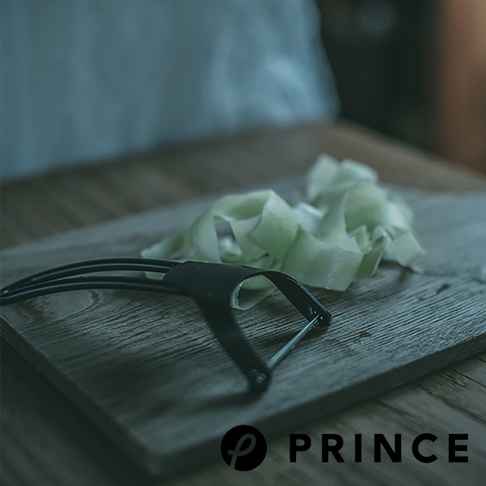 黑色削皮器，搭配淺綠色削皮的蔬菜，置於木質砧板上。