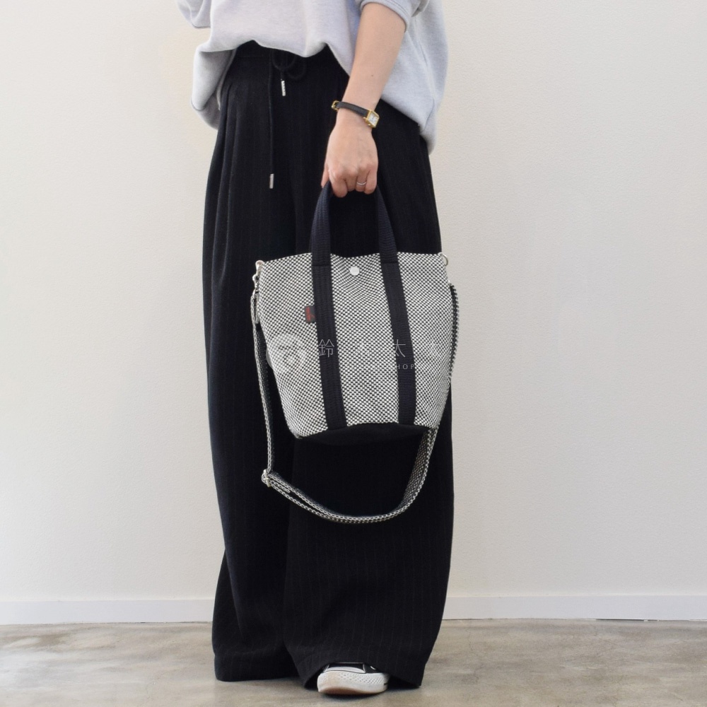 三河木綿刺子織兩用水桶包，黑白格紋主體，搭配黑色織帶提把與可拆卸肩帶，包身中央有品牌標誌。