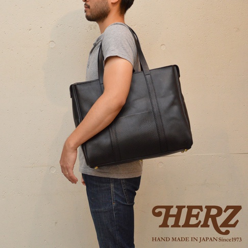 黑色皮革肩背拉鍊托特包，帶有外部貼袋和金色底部釘。