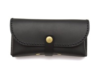 黑色皮革製成的職人手作眼鏡收納盒，附有金色按扣和皮革扣帶，邊緣有縫線裝飾。