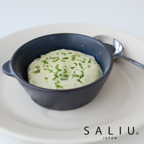 深灰色陶製圓鍋，內盛淺黃色馬鈴薯泥，撒有切碎的綠色香草，鍋子放在白色盤子上，旁有一支銀色湯匙。