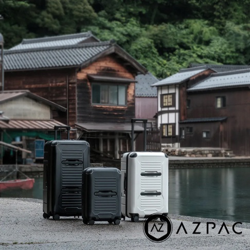 三個AZPAC Trucker 2.0 20吋煞車防爆行李箱，兩個黑色，一個白色，皆為硬殼材質，帶有伸縮拉桿和四個萬向輪。