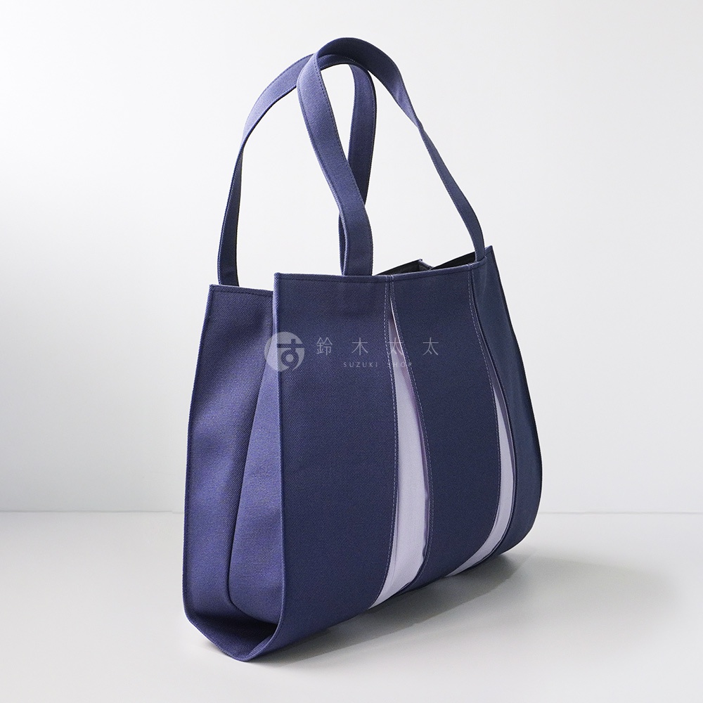 深藍色棉帆布扇形托特包，兩側有淺紫色布料拼接，配有兩條同色系的提把。