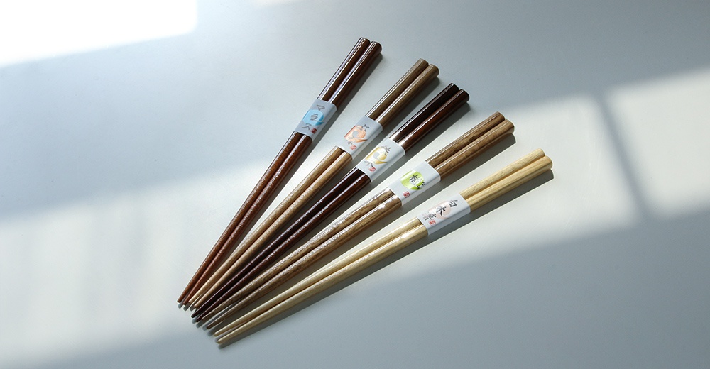五雙天然原色木筷，深淺不一的木質紋理，每雙筷子末端皆以印有圖案的紙帶綑綁。