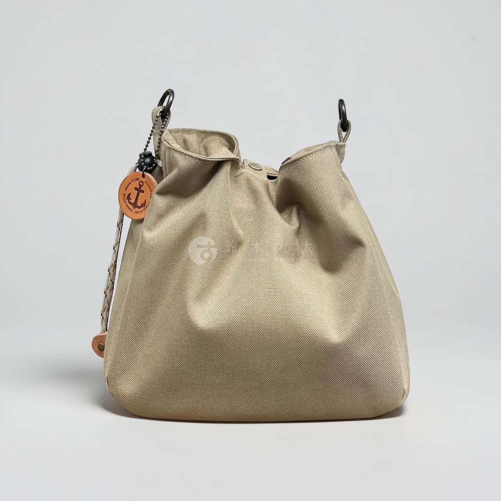 這是一個神戶clueto品牌的卡其色BALON mini多用途手提包，包身採用防潑水材質製成，外型簡約並帶有柔和的皺褶感，側面懸掛著印有船錨圖案的皮革吊飾，包口兩側裝有黑色金屬扣環，整體呈現出休閒且精緻的風格。