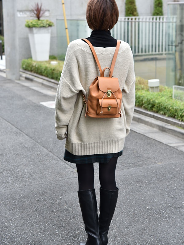 經典迷你後背包，焦糖色皮革材質，束口設計，正面有翻蓋式小口袋，配有金屬釦環與皮繩束帶，雙肩帶。