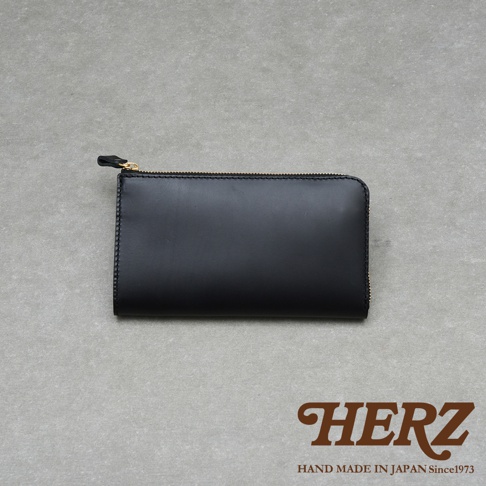 黑色皮革製的拉鍊長夾，上方有金色拉鍊，右下角有HERZ字樣和HAND MADE IN JAPAN Since1973字樣。