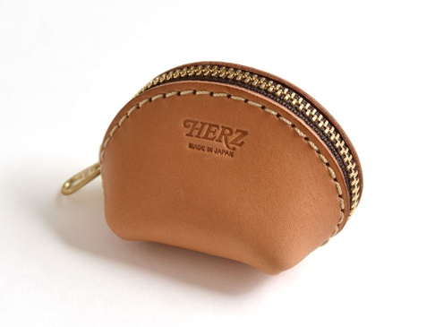 淺棕色職人手作皮革貝殼造型零錢包，配有黃銅色拉鍊和縫線，正面壓印有「HERZ」及「MADE IN JAPAN」字樣。