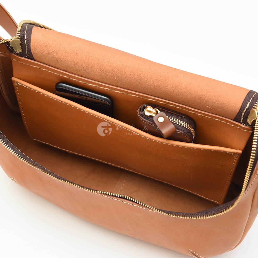 一個棕色皮革包的特寫，展示了內部結構，包括一個手機和一個小拉鍊零錢包，包的內襯為淺棕色。
