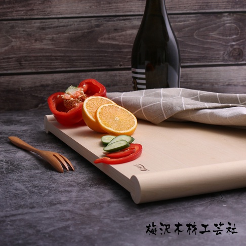 淺色木質砧板，上面擺放著紅甜椒、橘子片、小黃瓜片和紅辣椒片。一旁有木製叉子和一塊格子布，背景是深色木紋牆壁。