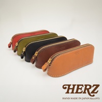 職人手作皮革三角弧形收納筆袋，展示紅色、綠色、黑色、棕色及駝色五種顏色，皆為真皮材質，配有金色拉鍊。