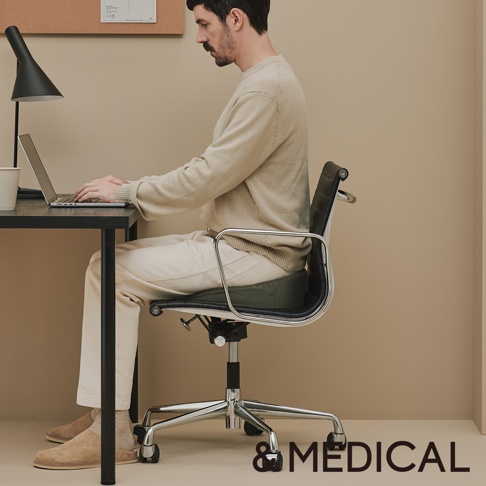 一名男性坐在辦公椅上，椅上有一個深綠色的低反發美姿支撐坐墊。