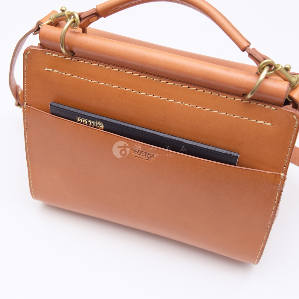 日本HERZ皮革側背包，特寫包前袋，露出黑色筆記本，上面有日文和英文標誌。