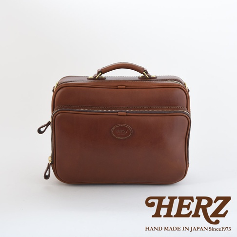 職人手作皮革兩用商務公事包，深棕色，光滑皮革材質，帶有金色拉鍊及提把，正面中央有一個圓形壓印品牌標誌。