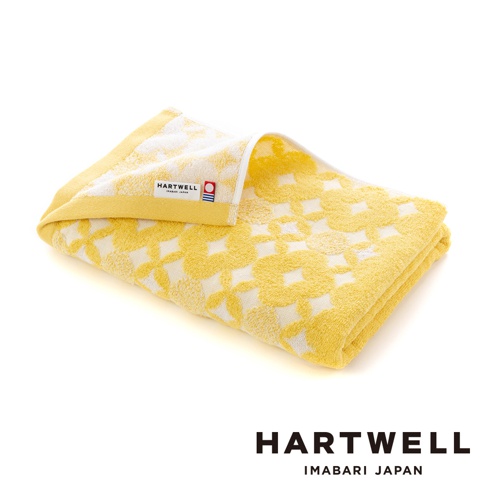 一條黃色毛巾，帶有白色傳統和風幾何紋樣，材質為棉，觸感柔軟。