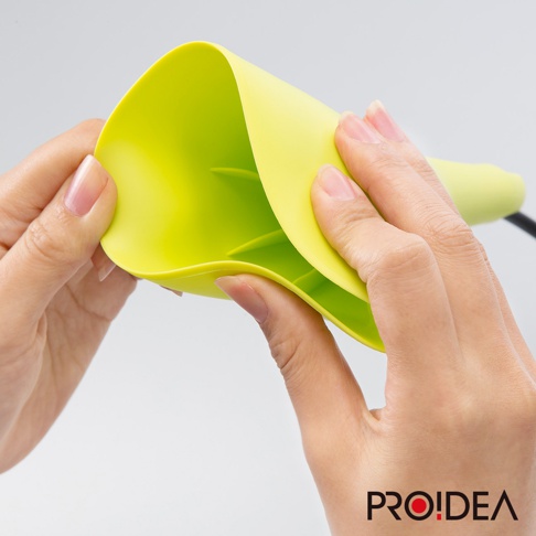 一雙手正拿起一個亮綠色的消音高歌器，其材質柔軟有彈性，內部有三個支架。