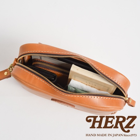 棕色皮革手提包，拉鍊半開，內部裝有錢包、書本和衣物。包包配有可拆卸扣環和縫線細節。